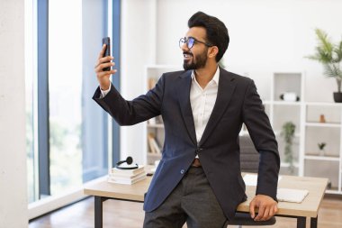 Arap bir işadamı modern ofis ortamında selfie çekerken gülümser.