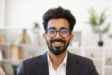 Bu portre, kameraya gülümseyen gözlüklü ve takım elbiseli kendine güvenen bir Hintli işadamını çekiyor.