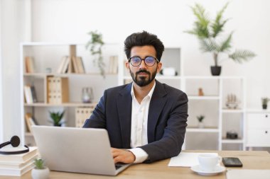 Hintli bir işadamı modern ofis ortamında dizüstü bilgisayarı üzerinde çalışıyor.