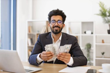 Hintli bir işadamı elinde bir tomar para tutarken gülümsüyor, finansal başarı ve zenginliği temsil ediyor.