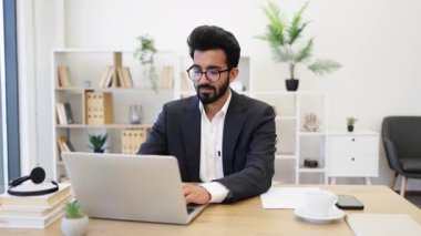 Hintli bir işadamı modern ofis ortamında dizüstü bilgisayarı üzerinde çalışıyor.