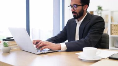 Hintli bir işadamı, modern bir ofis ortamında dizüstü bilgisayarıyla çalışıyor.