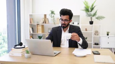 Hintli bir işadamı ofisinde bir fincan kahve tutarken gülümsüyor.