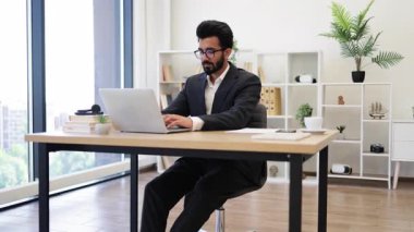 Hintli bir işadamı ofiste dizüstü bilgisayarı üzerinde çalışırken bir başarıyı kutluyor.