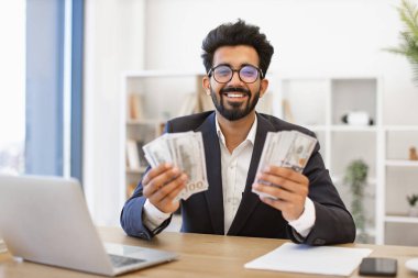Hintli bir işadamı elinde büyük miktarda para tutarken gülümsüyor ve mali başarıyı kutluyor.