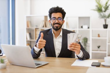 Hintli bir işadamı elinde para tutarken gülümser ve onayını gösterir.