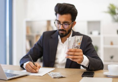 Hintli bir işadamı masasında para sayıyor ve notlar alıyor.