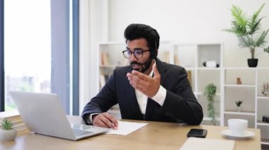 Kulaklık takan Arap bir işadamı bilgisayar kullanarak bir video konferans görüşmesine katılıyor.