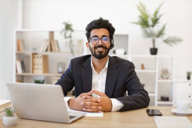 Hintli bir işadamı modern bir ofis ortamında masasında çalışırken gülümsüyor.