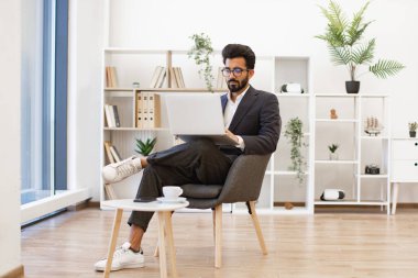 Arap bir işadamı, modern ofis ortamında dizüstü bilgisayarı üzerinde çalışıyor, odaklanmış ve profesyonel görünüyor.