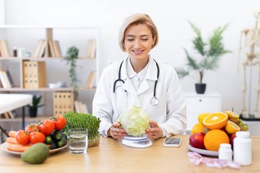 Gülümseyen bir beslenme uzmanı taze meyve ve sebzelerle çevrili bir lahanayı tartarak sağlıklı beslenme alışkanlıklarını teşvik eder..