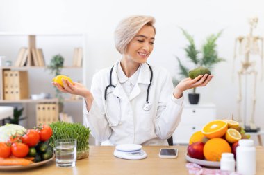 Gülümseyen bir diyetçi taze ürünlerle çevrili bir limon ve avokado tutar, sağlıklı beslenmeyi ve beslenmeyi teşvik eder..