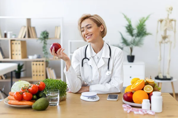 Gülümseyen bir diyetçi taze ürünlerle çevrili bir elma tutar, sağlıklı beslenmeyi ve sağlığı teşvik eder..