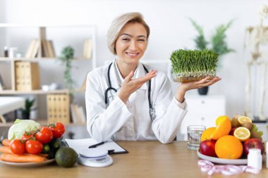 Beyaz önlüklü gülümseyen bir beslenme uzmanı taze lahanalar, çeşitli meyve ve sebzeler sunarak sağlıklı beslenmeyi teşvik ediyor..