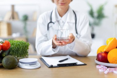 Elinde taze meyve ve sebzelerle çevrili bir bardak su tutan bir doktor sağlıklı bir yaşam tarzını teşvik ediyor..