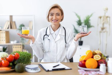 Gülümseyen bir beslenme uzmanı iki bardak sunar, biri meyve suyu, diğeri su, sağlıklı beslenme ve yaşam tarzı tercihleri sunar..