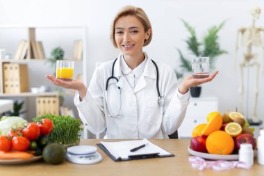 Gülümseyen bir diyetçi meyve ve sebzelerle çevrili bir bardak su ve meyve suyu tutarak sağlıklı yeme alışkanlıklarını teşvik eder..