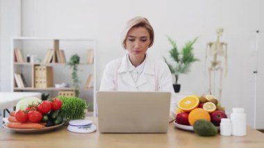 Taze meyve ve sebzelerle çevrili bir dizüstü bilgisayar üzerinde çalışan bir beslenme uzmanı sağlıklı yeme alışkanlıklarını teşvik ediyor..