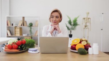 Diyetisyen bir masada dizüstü bilgisayarla oturuyor, yeni ürünler ve takviyelerle çevrili, bir sonraki hamlesini düşünüyor..