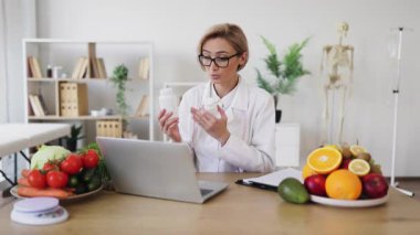 Bir beslenme uzmanı, elinde meyve ve sebzelerle birlikte destek şişeleriyle çevrimiçi danışmanlık yapıyor..