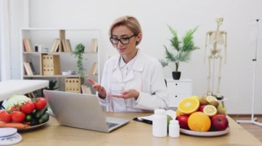 Bir kadın beslenme uzmanı, sağlıklı gıda ve takviyelerle çevrili bir hastaya çevrimiçi danışmanlık yapar..
