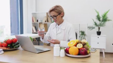 İnternette bir müşteriyle diyet danışmanlığı yapıyor, bir bardak su tutuyor ve sağlıklı yiyeceklerle çevrili..