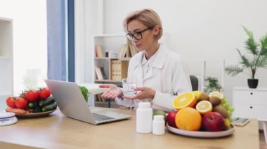Beyaz önlüklü bir diyetçi, çevresi meyve, sebze ve takviyelerle çevrili bir hastayla çevrimiçi olarak görüşür..