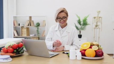 İnternette bir müşteriyle diyet danışmanlığı yapıyor, elinde avokado tutuyor ve etrafı taze meyve ve sebzelerle çevrili..