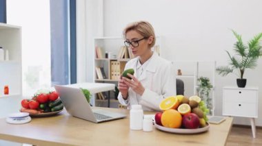 Bir beslenme ve sağlıklı beslenme alışkanlıklarını tartışırken elinde avokado tutan bir müşteriyle diyet danışmanlığı yapıyor..