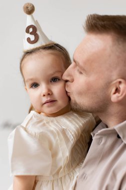 Sevgi dolu bir baba, küçük kızını yanağından öper. O da doğum günü şapkası takar ve üçüncü doğum gününü kutlar..