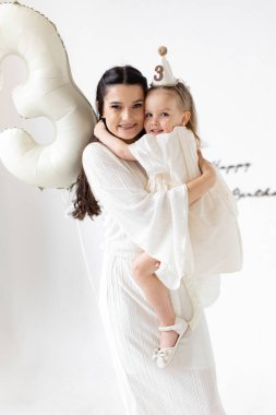 Bir anne, üçüncü doğum gününü balon ve parti şapkasıyla kutlar..
