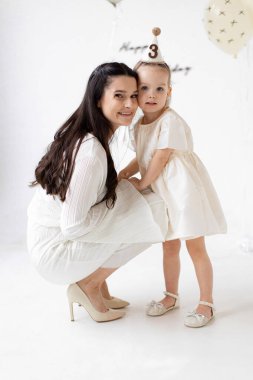 Bir anne ve küçük kızı birlikte bir doğum günü kutluyorlar, kızı parti şapkası takıyor..