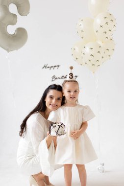 A heartwarming scene of a mother and her young daughter celebrating a birthday with a cake and balloons.