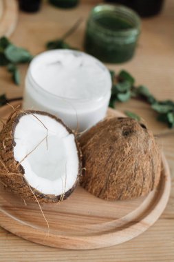 Yarım hindistan cevizi bir kavanoz beyaz krema ve yeşil yaprakların yanına oturur. Bu da doğal cilt bakımı olduğunu gösterir.