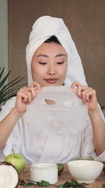 Beyaz bornoz ve havlu giymiş genç bir kadın cilt bakımı ve güzellik tedavisi için maske takıyor.