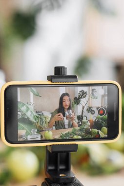 Genç bir kadın, çevrimiçi izleyicileri için taze malzemelerle sağlıklı bir yemek hazırlarken kendini filme çekiyor.