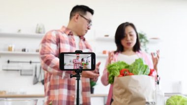 Bir çift, parlak mutfaklarında pişirme videosu için taze malzemeler hazırlıyor.