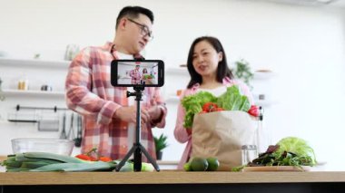 Bir çift, parlak mutfaklarında yemek pişirme videosu için taze sebzeler hazırlıyor.