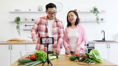 Asyalı bir çift çevrimiçi izleyicileri için yemek videosu çekerken birlikte yemek hazırlıyor.