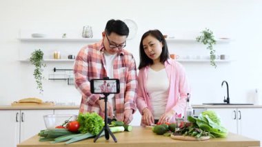 Asyalı bir çift, çevrimiçi izleyicileri için video çekerken mutfakta yemek hazırlıyor.