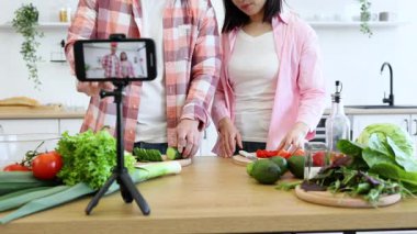 Bir çift mutfağındaki bir video bloğunu kameraya çekiyor. İşlemi kaydetmek için tripoda akıllı telefon takıyorlar.