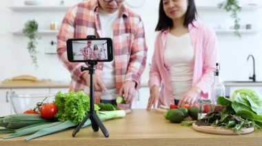Bir aile mutfakta, sağlıklı bir yemek için taze sebze hazırlayan bir yemek videosu çekiyor.