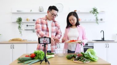 Asyalı bir çift, çevrimiçi izleyicileri için video çekerken mutfakta yemek hazırlıyor.