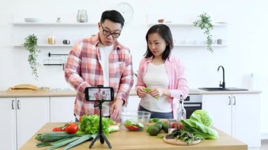 Asyalı bir çift, çevrimiçi izleyicileri için video çekerken mutfağında sağlıklı bir yemek hazırlıyor.