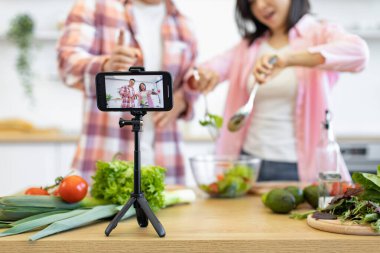 Bir çift mutfağında taze sebzeli sağlıklı bir salata hazırlayan bir video kaydediyor.