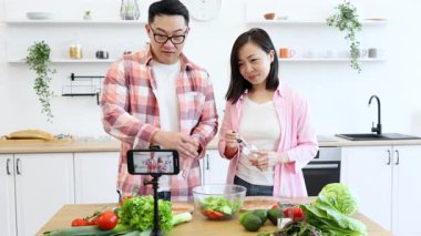 Asyalı bir çift, takipçileri için video çekerken mutfakta salata hazırlıyor.