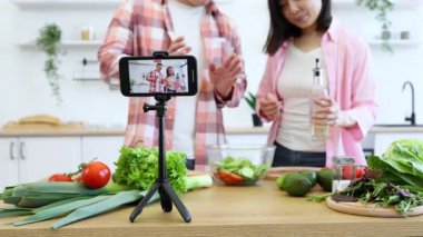 Bir çift mutfağında bir yemek videosu çekiyor, sağlıklı malzemelerle taze bir salata hazırlıyorlar.