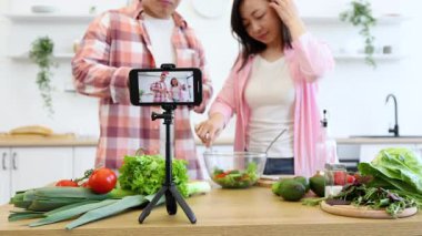 Bir çift, çevrimiçi izleyicileri için video çekerken mutfakta taze bir salata hazırlıyor.