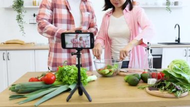 Bir çift mutfağında taze sebzeli sağlıklı bir salata hazırlayan bir video kaydediyor.