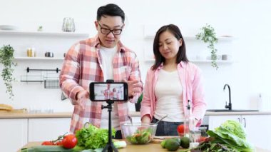 Mutlu bir çift mutfağında taze sebzeleri eğlence için kullanarak yemek videosu çekiyor.